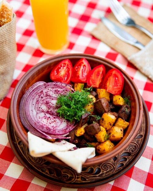 Carne frita con papas servidas con cebolla, tomates y verduras.