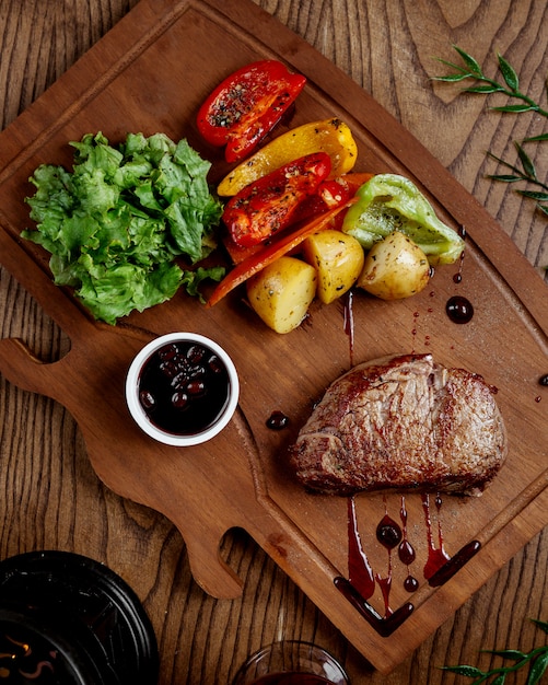 Carne frita con papas y verduras sobre tabla de madera