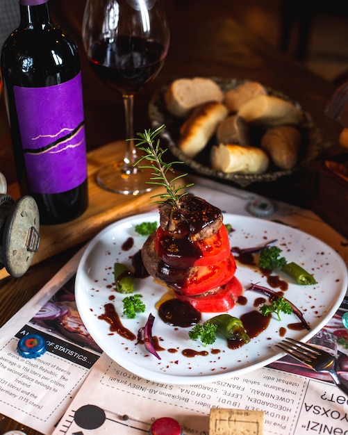 Carne frita con rodajas de tomate, verduras, salsa, ramita de romero servida con vino.