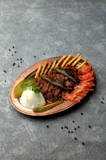 Carne frita servida con rodajas de tomate, papas fritas y encurtidos.