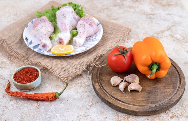 Carne de muslos de pollo sin cocer con verduras sobre una tabla de madera