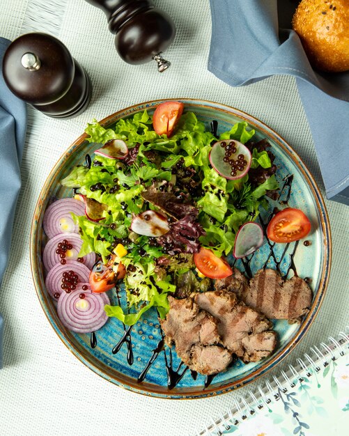 carne a la parrilla con ensalada de verduras y cebolla en una bandeja