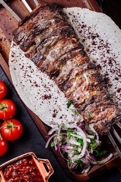 Carne a la parrilla sobre pan lavash con ensalada de cebolla y hierbas.