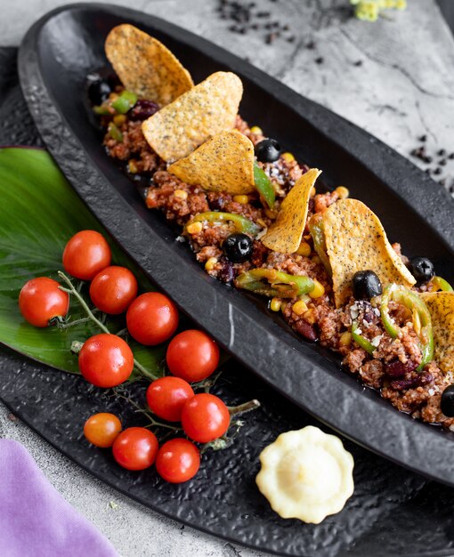 Carne picada servida con pimienta de maíz, aceitunas y chips de tortilla