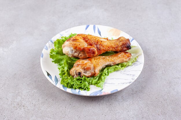 Carne de piernas de pollo a la parrilla con lechuga en la placa blanca.