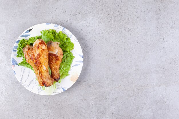 Carne de piernas de pollo a la parrilla con lechuga en la placa blanca.