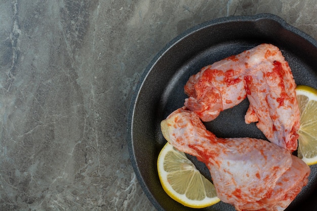 Carne de pollo cruda con especias y limón en sartén oscura. Foto de alta calidad