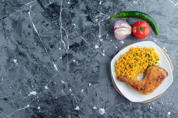 Carne de pollo y fideos en un plato sobre un salvamanteles junto a verduras, sobre el fondo de mármol.