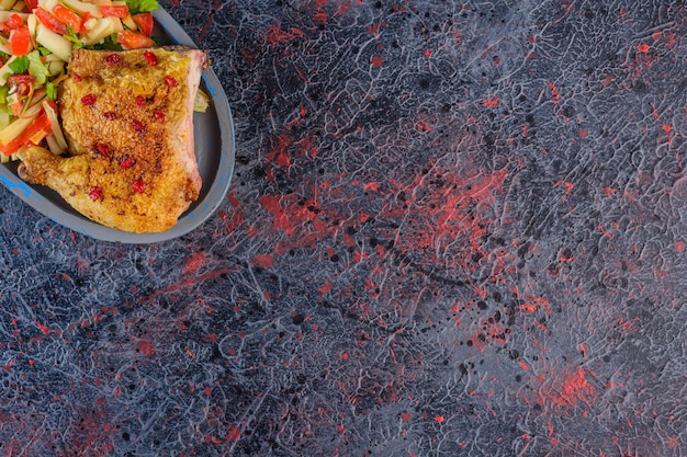 Carne de pollo frito con ensalada de verduras mixtas sobre una superficie oscura