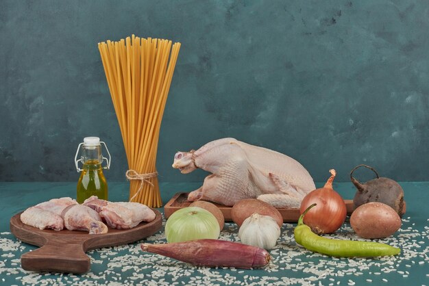 Carne de pollo sobre una tabla de madera con pasta y verduras alrededor.