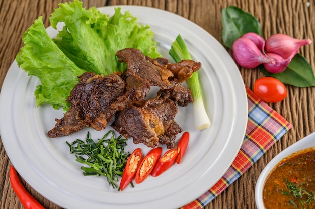 Carne de res frita comida tailandesa en un plato blanco con cebolleta, hojas de lima kaffir, chiles, ensalada, cebolla roja y tomates.