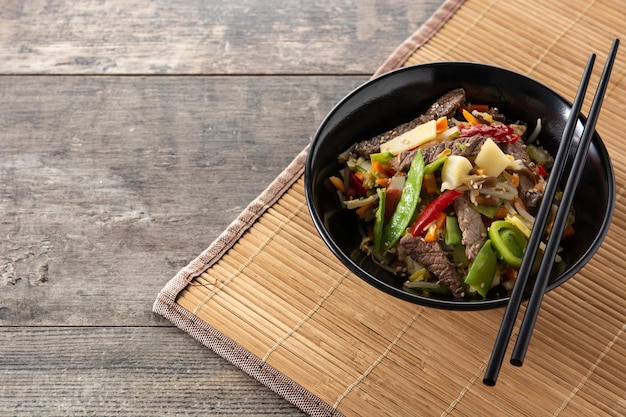 Carne de res, verduras y semillas de sésamo en un tazón negro sobre una mesa de madera