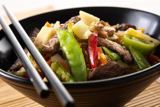 Carne de res, verduras y semillas de sésamo en un tazón negro sobre una mesa de madera