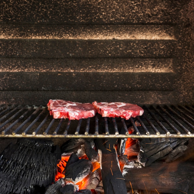 Carne roja sin procesar en el hoyo de la parrilla con briquetas de carbón calientes