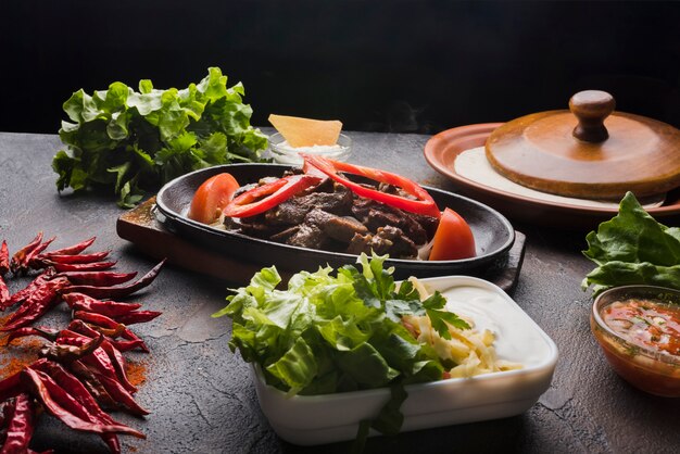 Carne, verduras y aperitivo en mesa de madera.