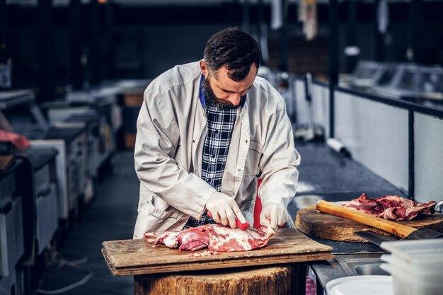 Carnicero barbudo vestido con una camisa de lana corta carne de tocino fresco.