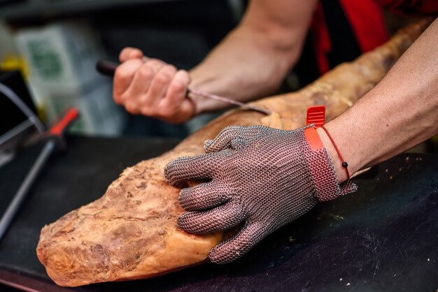 Carnicero deshuesando un jamón con malla metálica de seguridad.