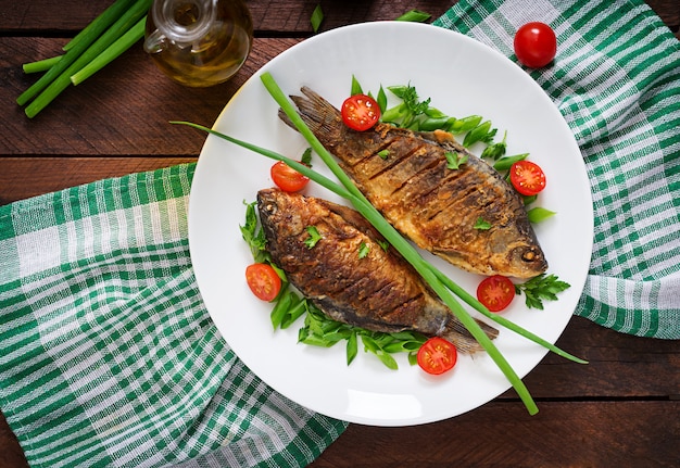 Carpa de pescado frito y ensalada de verduras frescas en la mesa de madera. Endecha plana. Vista superior