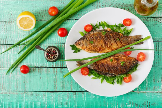 Carpa de pescado frito y ensalada de verduras frescas en la mesa de madera. Endecha plana. Vista superior