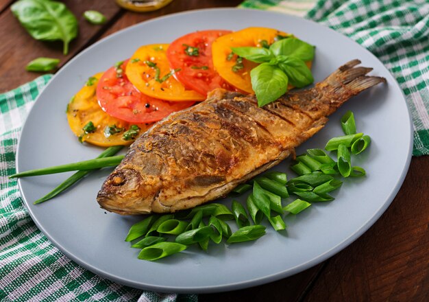 Carpa de pescado frito y ensalada de verduras frescas en la mesa de madera.