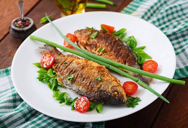 Carpa de pescado frito y ensalada de verduras frescas en la mesa de madera.