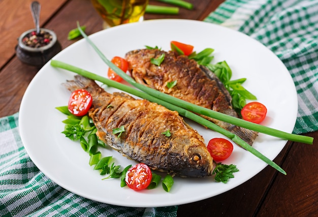 Carpa de pescado frito y ensalada de verduras frescas en la mesa de madera.