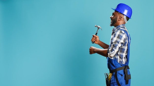 Foto gratuita carpintero afroamericano golpeando paredes con martillo, usando instrumentos manuales para trabajos de renovación y reconstrucción. constructor masculino en overoles con herramienta de salmonete de martillo neumático.