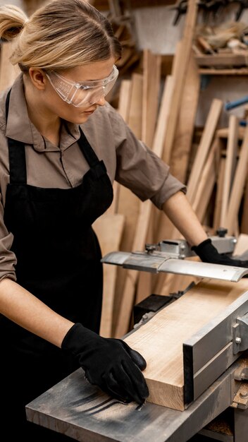 Carpintero femenino con gafas de seguridad para aserrar madera