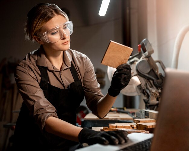 Carpintero femenino con gafas de seguridad mirando un trozo de madera en el estudio.