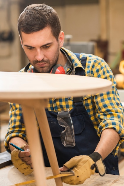 Foto gratuita un carpintero macho midiendo la mesa de madera con regla