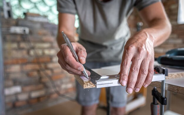 El carpintero mide la madera con una herramienta angular y toma notas.