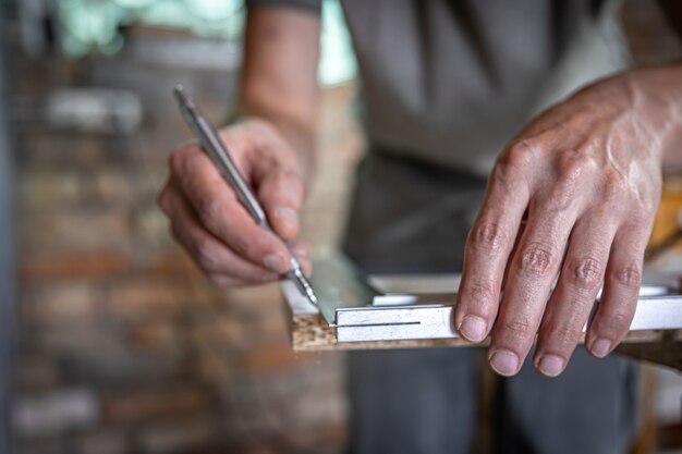 El carpintero mide la madera con una herramienta angular y toma notas.