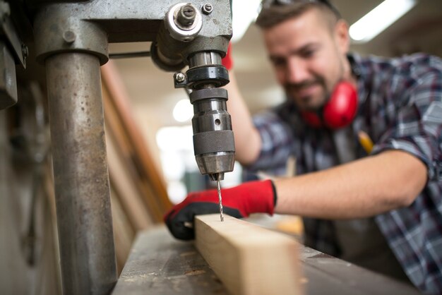 Carpintero profesional trabajador que perfora material de madera con taladro vertical