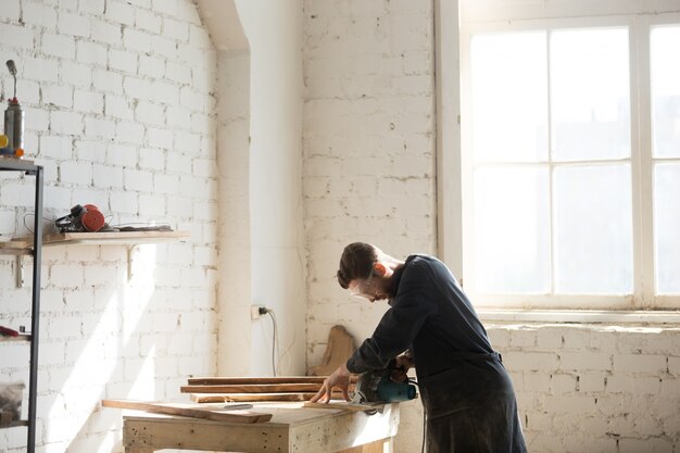 Carpintero profesional utilizando poder mano vio en el taller, vista lateral
