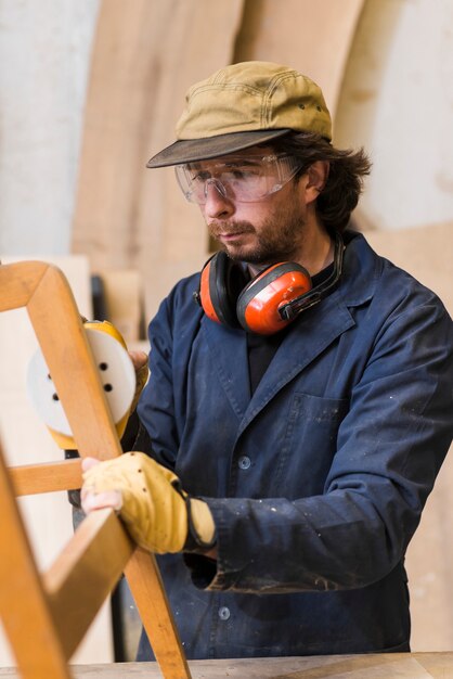 Carpintero puliendo muebles de madera con una lijadora de órbita al azar en el taller