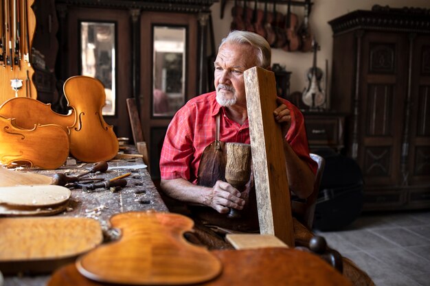 Carpintero senior artesano comprobando la calidad del sonido del material de madera en su antiguo taller de carpintero