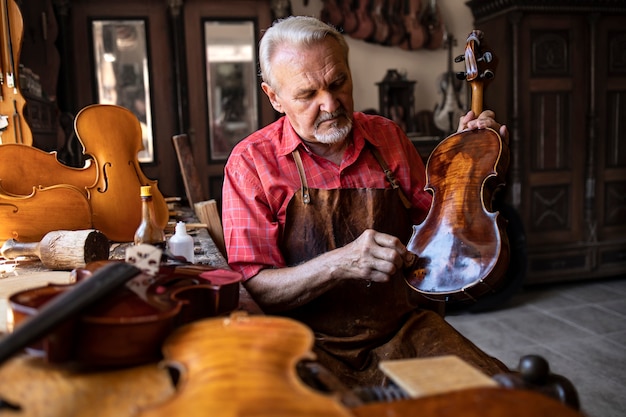 Foto gratuita carpintero senior artesano pulido instrumento de violín en su taller de carpintero