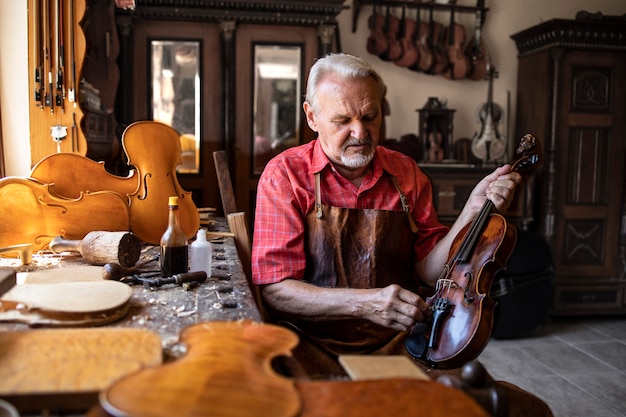 Foto gratuita carpintero senior artesano pulido instrumento de violín en su taller de carpintero