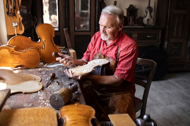 Carpintero senior artesano tallando madera y haciendo instrumento de violín