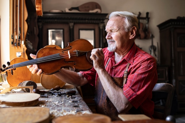 Foto gratuita carpintero senior comprobando el instrumento de violín que está a punto de reparar