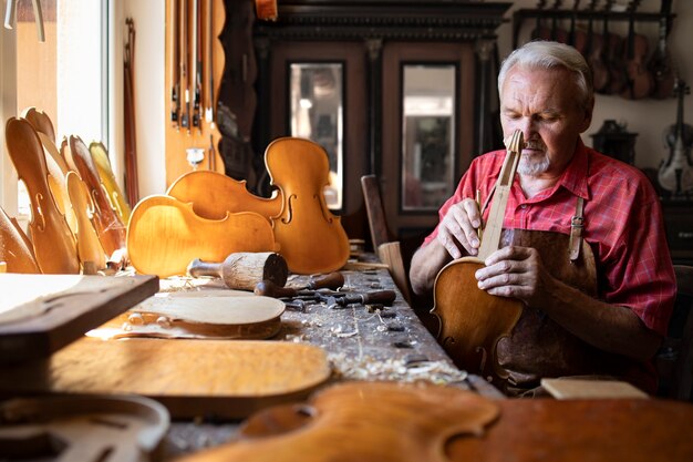 Carpintero senior ensamblar piezas de violín en su taller de carpintero
