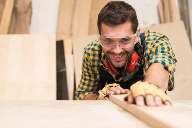 Foto gratuita un carpintero de sexo masculino feliz que ajusta el tablón de madera en el taller