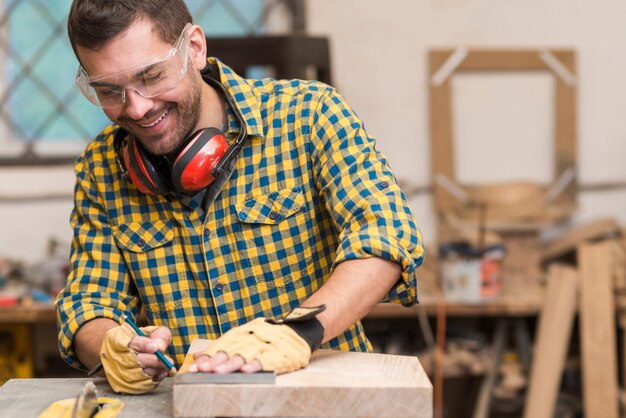 Carpintero de sexo masculino joven sonriente que trabaja con madera en su taller