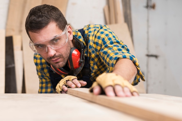 Un carpintero de sexo masculino que coloca el tablón en superficie de madera en el taller