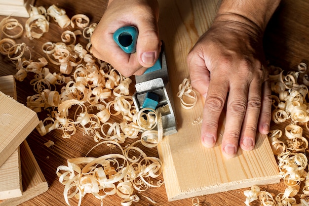 Carpintero trabajando en madera rodeada de aserrín