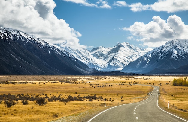 Carretera asfaltada a través del campo con montañas cubiertas de nieve en el fondo