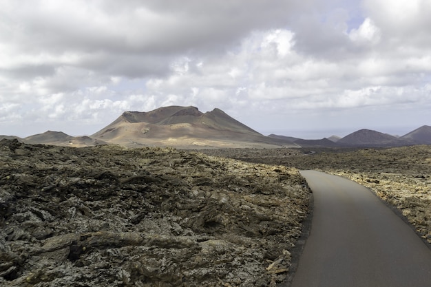 Carretera con curvas rodeada de colinas bajo un cielo nublado en el parque nacional de timanfaya en españa
