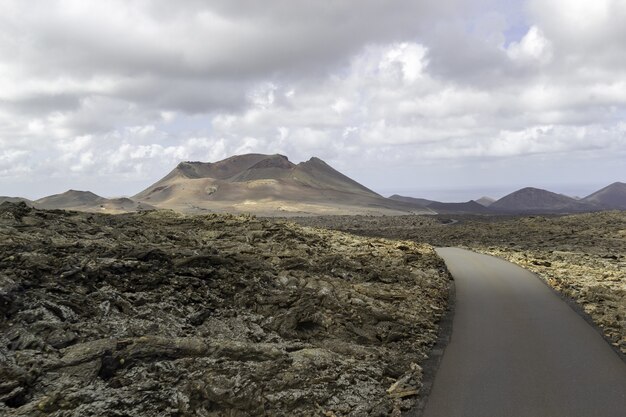 Carretera con curvas rodeada de colinas bajo un cielo nublado en el Parque Nacional de Timanfaya en España