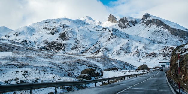 Carretera estrecha rodeada de altas montañas rocosas cubiertas de nieve bajo un cielo nublado