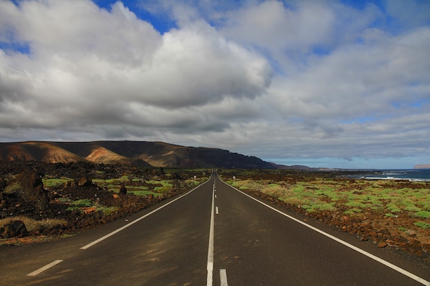 Carretera en medio de un campo de hierba con una montaña en la distancia bajo un cielo nublado